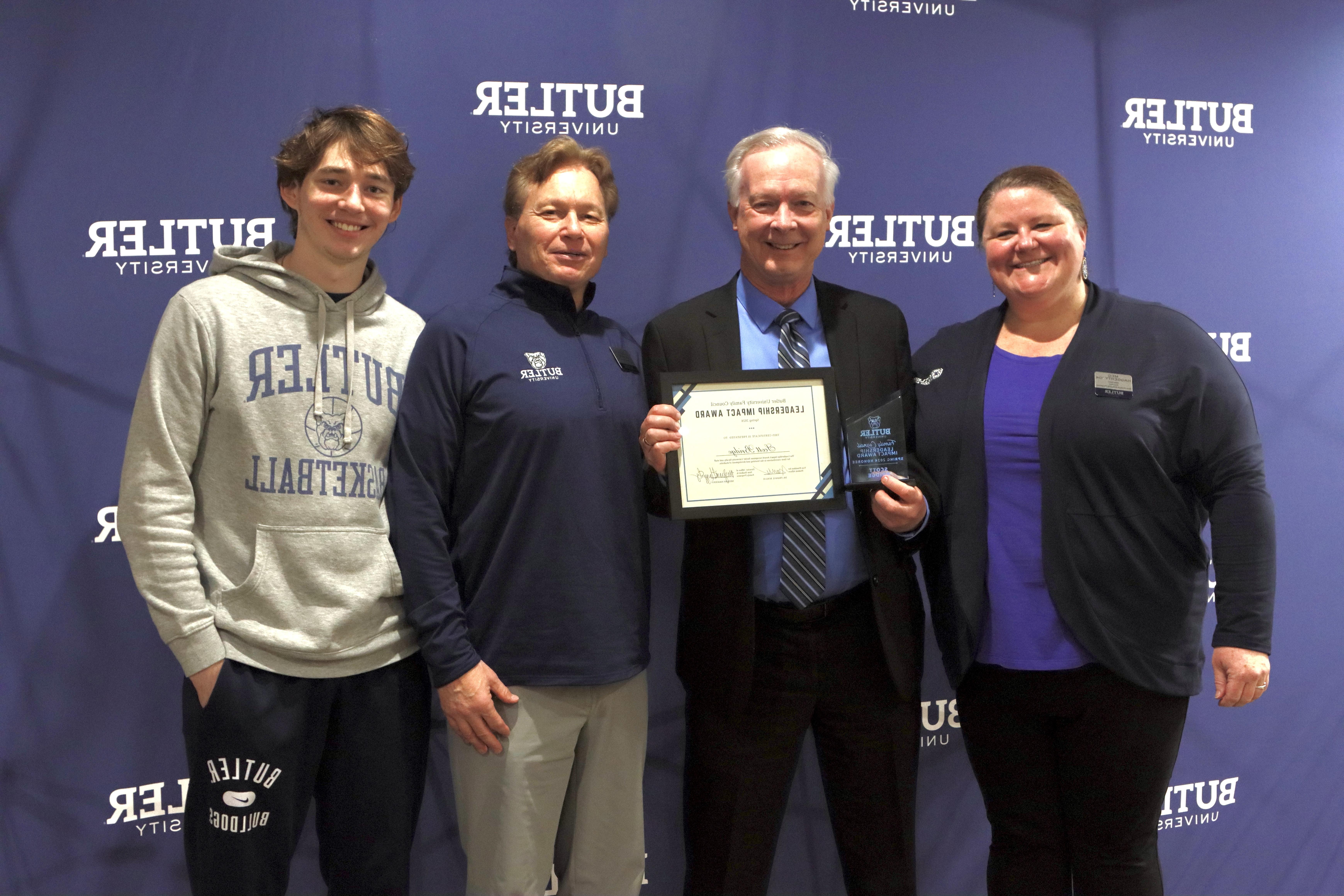 Professor Scott Bridges poses with his certificate and trophy alongside Director of New Student & Family Programs Meg Haggerty (left) and nominating family Glen Danahey and student Brock Danahey (right). Butler University backdrop with four people posing in front. Scott Bridge holding his certificate and trophy.